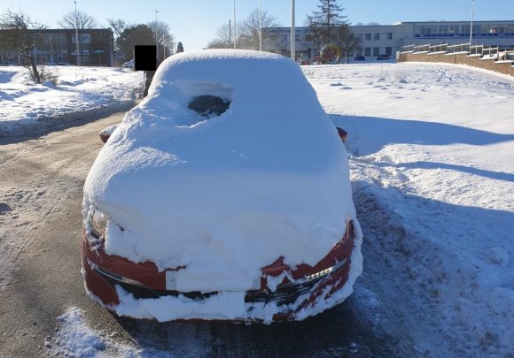 A car covered in snow with a small window for the driver to see out of